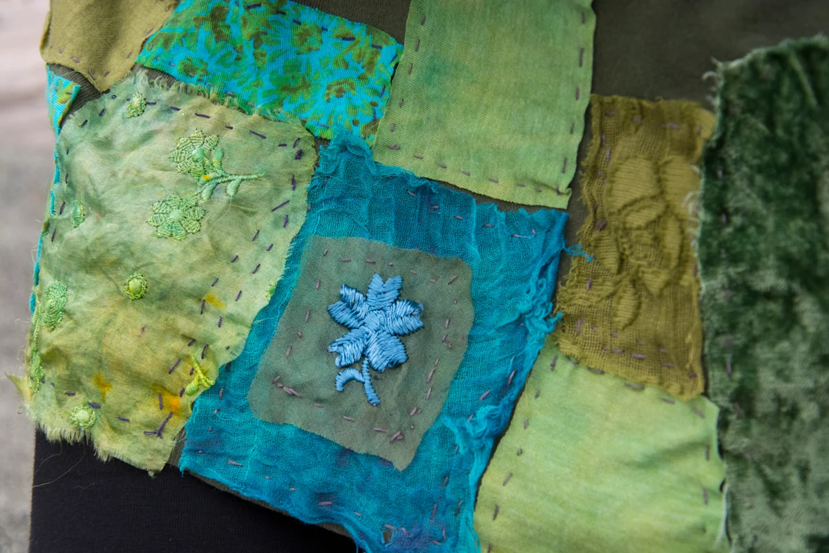 Green and turquoise patchwork with visible stitching and a small blue floral embellishment.