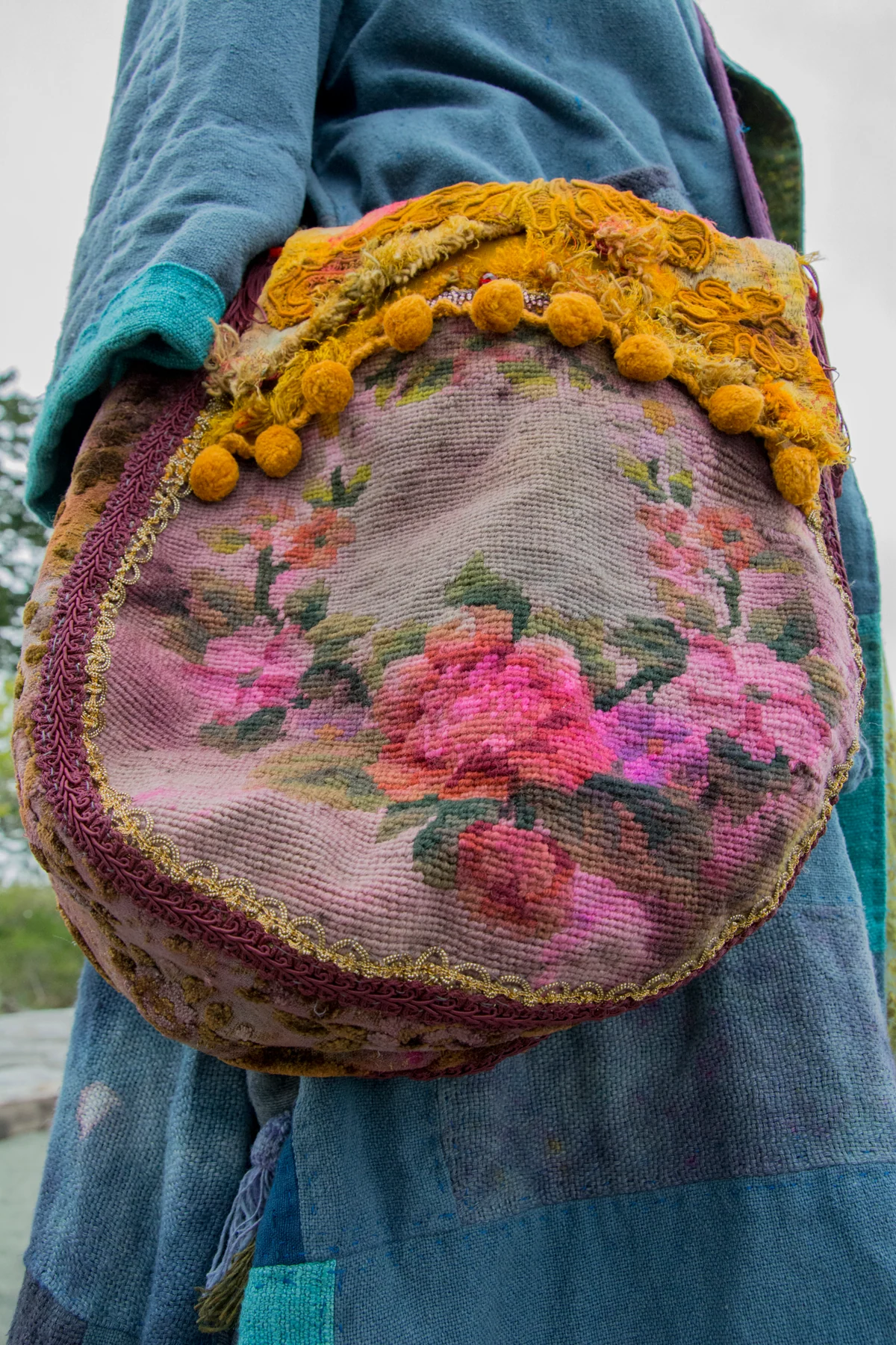 Round textile bag with pink floral embroidery and thick yellow fibre trim.