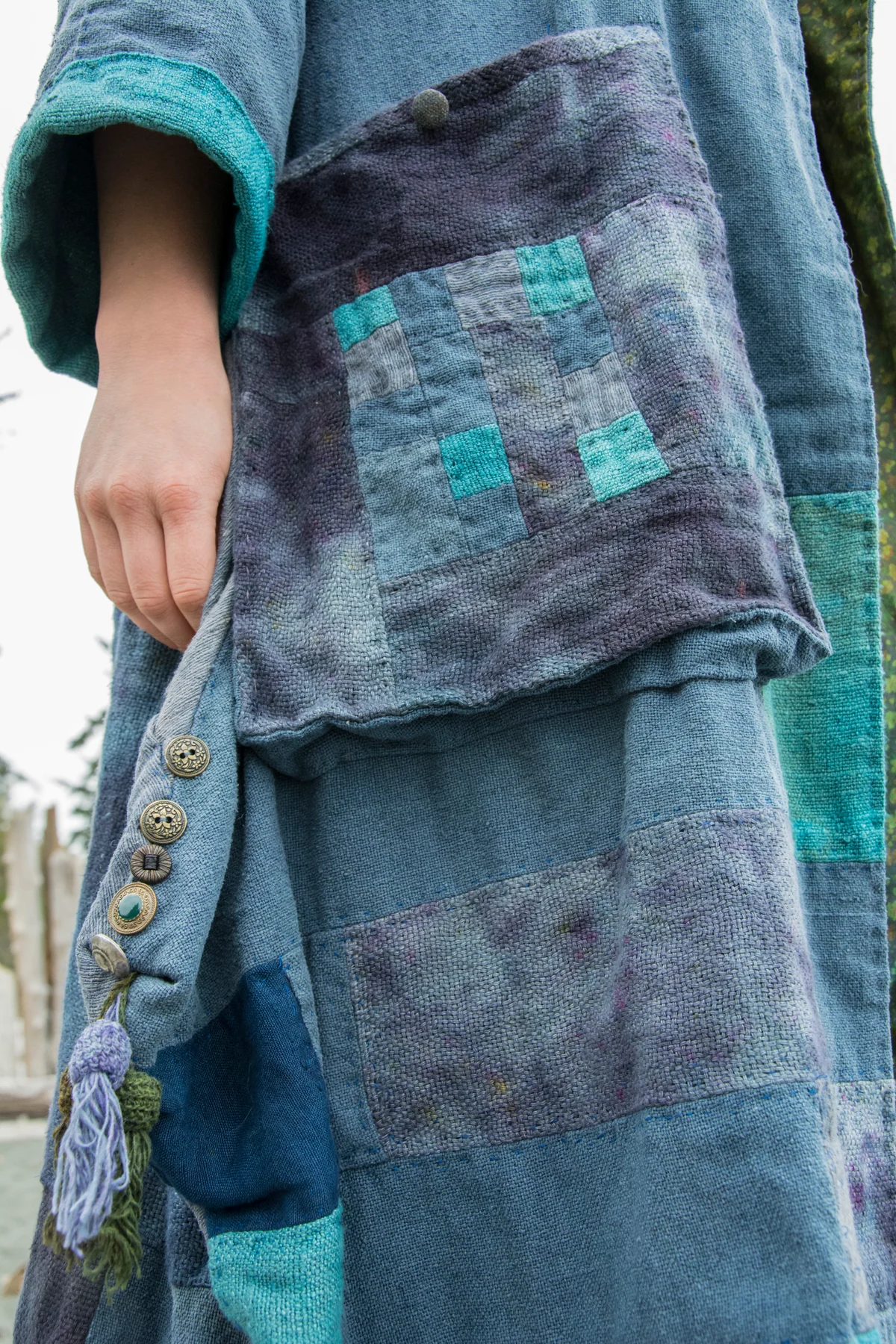 Close view of a blue garment with layered square patchwork pockets and fabric-covered buttons.
