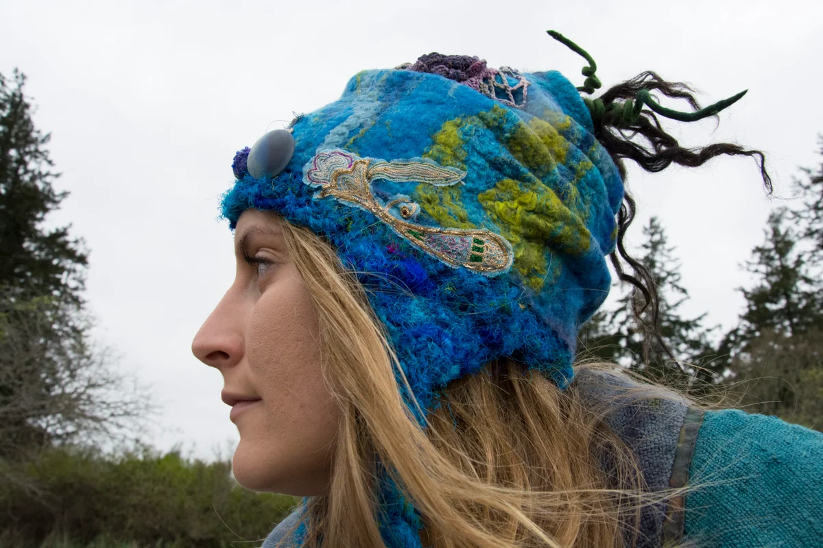 Model wearing a blue and green textured fibre hat with layered textile embellishments.