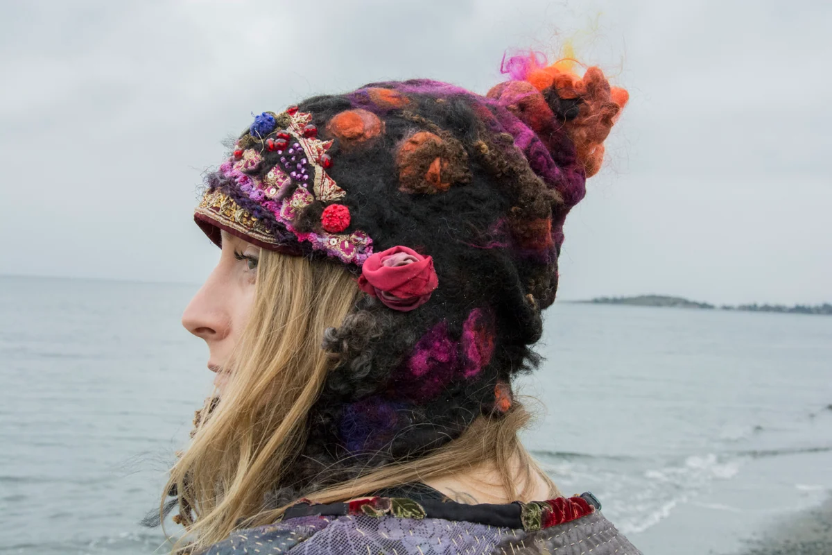 Side view of a model wearing dark fibre headwear with pink, orange and patterned embellishments.