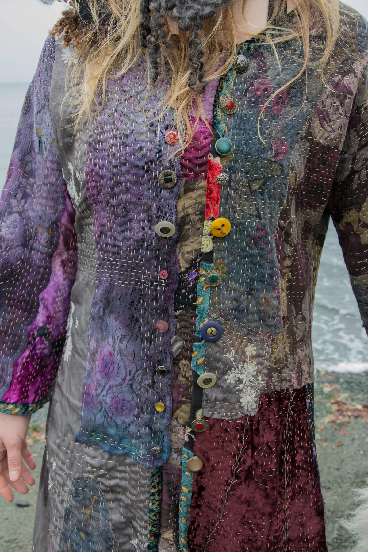 Purple, grey and burgundy garment panels with visible running stitches and colourful buttons.