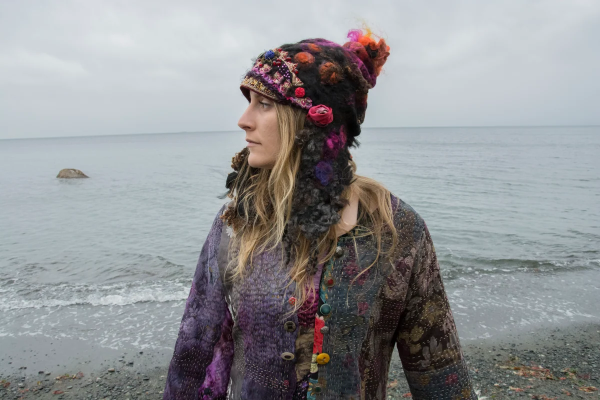 Dana Sitar’s layered purple and burgundy wearable fibre work photographed on a model beside the sea.
